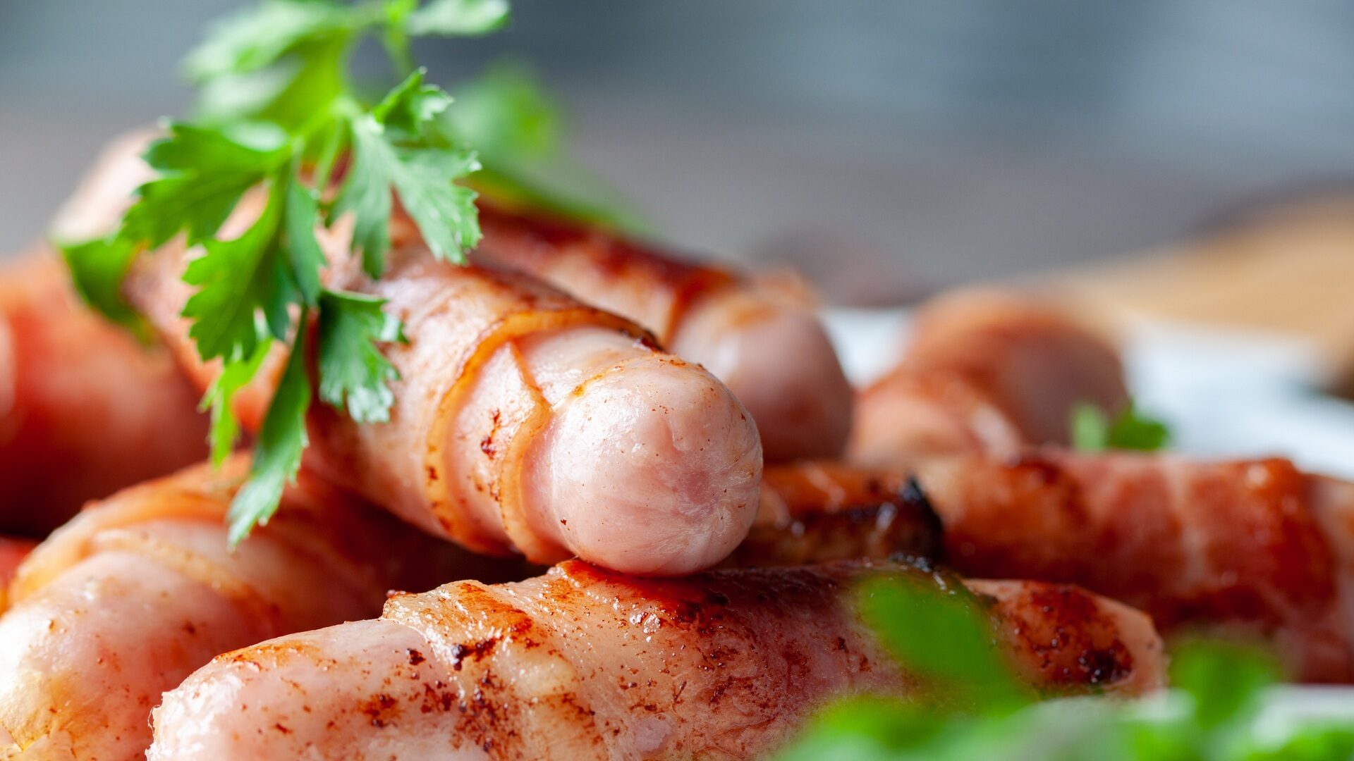 Grilled wrapped bacon sausages on white plate.